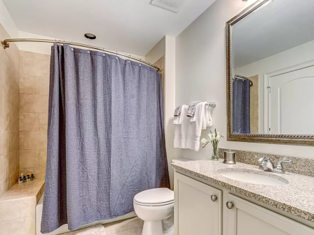 A clean bathroom features a shower with a blue curtain, granite countertop sink, towels, and a large mirror.