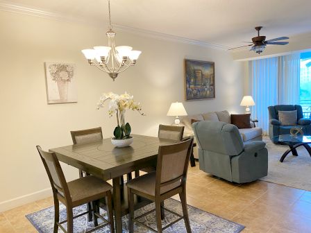 A cozy living room and dining area with a table, chairs, sofa, armchairs, paintings, and decorative lighting.