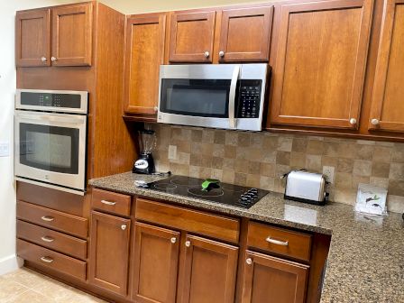 A kitchen with wooden cabinets, double oven, microwave, blender, toaster, and electric stovetop on a granite countertop.