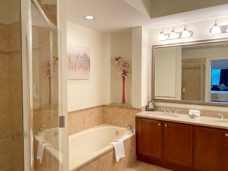 This image shows a bathroom with a bathtub, shower, vanity with dual sinks, a large mirror, artwork, and decorative flowers.