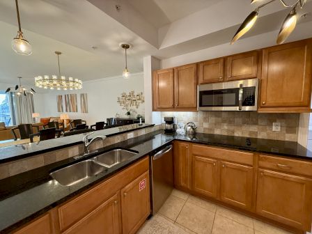 A modern kitchen with wooden cabinets, stainless steel appliances, and a double sink, leading to a dining area with stylish decor.