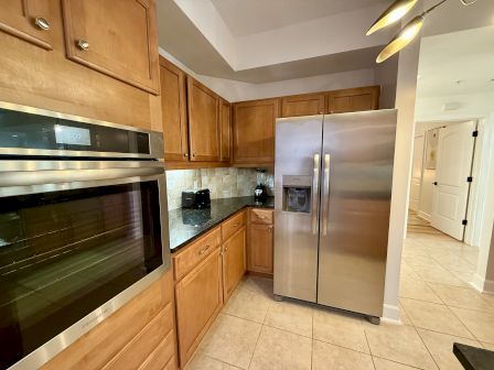 A kitchen with wooden cabinets, stainless steel fridge, wall oven, countertops, toaster, and tile flooring.