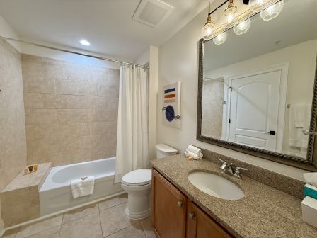 A clean, modern bathroom with a granite countertop, large mirror, bathtub with a shower curtain, and abstract wall art.