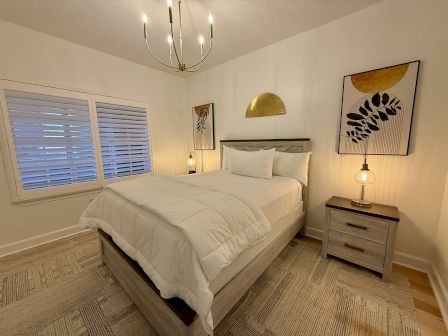 A cozy bedroom with a neatly made bed, decorative wall art, bedside lamps on nightstands, and a stylish chandelier.
