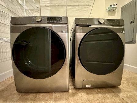 The image shows two Samsung front-loading laundry machines side by side, on a tiled floor in a laundry room.