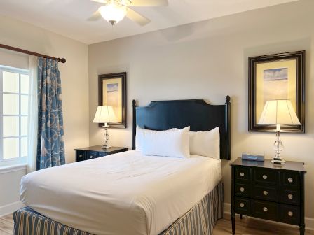 A bedroom with a bed, two lamps on bedside tables, nautical curtains, and framed artwork above the lamps.