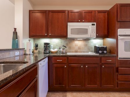 A kitchen with wooden cabinets, granite countertops, a microwave, oven, toaster, coffee maker, kettle, and a sink area is shown.