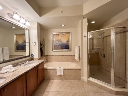 A modern bathroom with a large mirror, sink, bathtub, glass shower, and decorative painting on the wall.