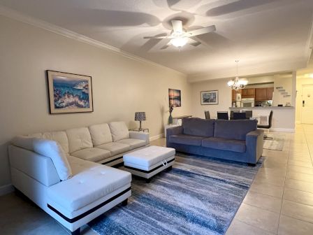 A spacious living room with a white sectional sofa, gray couch, blue rug, paintings on the wall, and a dining area in the background.