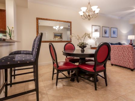 A modern dining area with a round table, red chairs, bar stools, overhead lighting, and decorative elements in a cozy room.