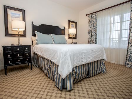 A neatly arranged bedroom with a bed, two lamps, a nightstand, and decorative curtains and pictures.