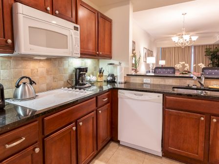 A modern kitchen with wooden cabinets, granite countertops, appliances, a kettle, coffee maker, dishwasher, and a view into the dining area.