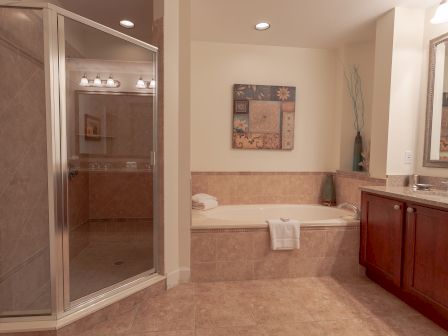A bathroom with a glass shower, a large bathtub, a wooden vanity, and decorative art on the wall.