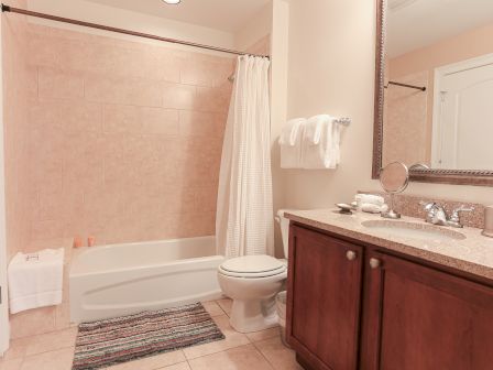 A bathroom with a bathtub, shower curtain, toilet, towels on racks, large mirror, and a countertop with a sink and toiletries.