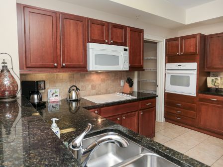 A modern kitchen with dark countertops, wooden cabinets, a stove, microwave, sink, coffee maker, and a lantern. Fully equipped and tidy.