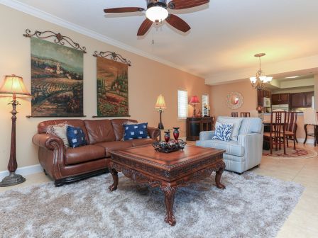 A cozy living room with a brown leather sofa, artwork on the wall, and elegant decor, connected to an open dining area and kitchen.