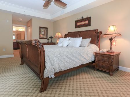 A cozy bedroom with a wooden bed, patterned bedding, bedside tables, lamps, and a ceiling fan in a warmly lit setting.