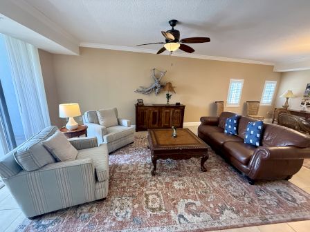 A cozy living room with a ceiling fan, two armchairs, a leather sofa, wooden coffee table, and decor on beige walls.