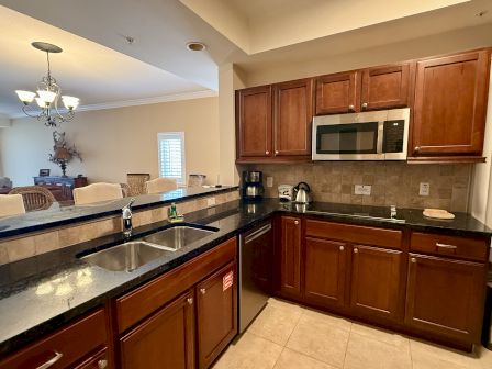 A modern kitchen with brown cabinets, granite countertops, a microwave, and a sink, opening into a dining area.