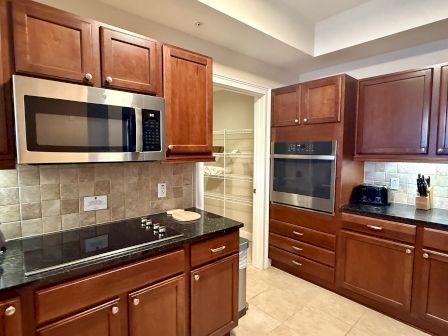 A kitchen with wooden cabinets, a microwave, an oven, a stovetop, and a small countertop appliance is shown in the image.