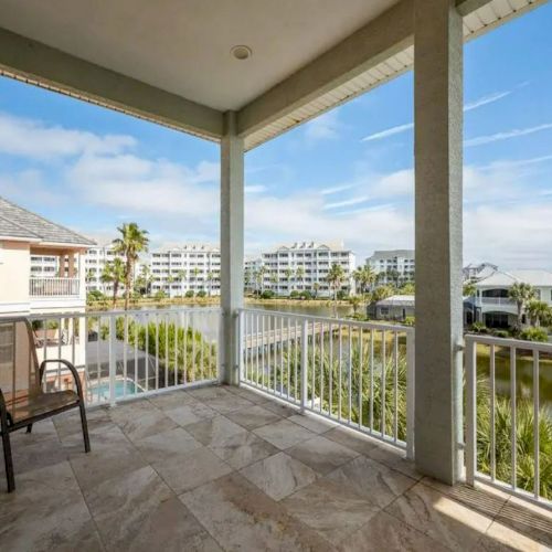 A patio with a chair overlooks a scenic view of buildings, palm trees, and water, under a partly cloudy sky.