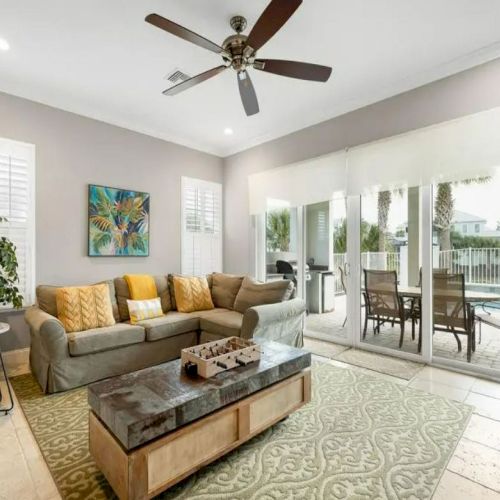 A cozy living room with a gray sofa, patterned rug, and coffee table, opening to a patio and pool area through large sliding doors.