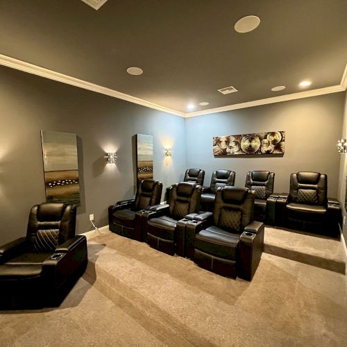 A home theater room with tiered seating, recliners, wall sconces, and modern decor, creating a cozy and luxurious viewing experience.