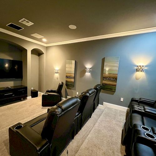 A home theater room with several reclining leather chairs, a large screen, and wall decor, dimly lit for a cozy ambiance.