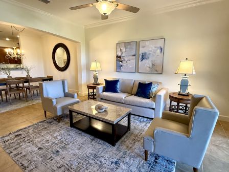 A modern living room with a sofa, armchairs, lamps, abstract art, and a coffee table. A dining area is seen in the background.