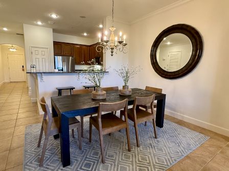 A dining area with a dark table, wooden chairs, a vase with plants, a chandelier, and a large round mirror on the wall.