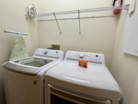 A laundry room with a washer, dryer, ironing board, iron, shelf with a fire extinguisher, and a box of Tide detergent on the dryer.