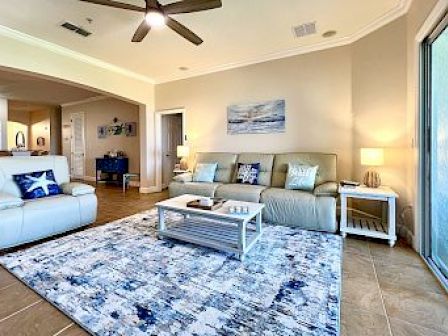 A modern living room with a beige couch, patterned rug, coffee table, and sliding glass door, featuring blue and white decor.