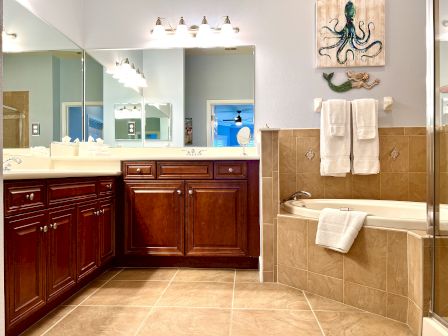 A bathroom with wooden cabinets, large mirrors, a bathtub with towels, and ocean-themed decor on the wall.