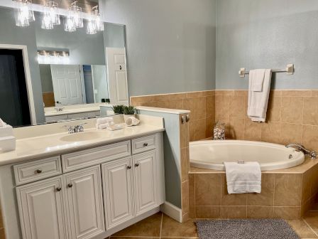 A clean bathroom with a white vanity, large mirror, and a bathtub with beige tiles. Towels and decor are neatly arranged.