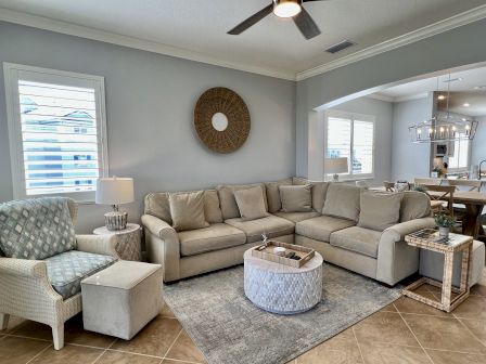 The image shows a cozy living room with a beige sectional sofa, patterned armchair, and a stylish coffee table, leading into a dining area.