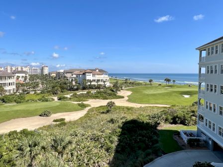 A coastal golf course with residential buildings and the ocean in the background under a clear blue sky.