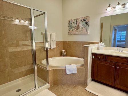 A bathroom with a glass-enclosed shower, corner bathtub, sink with wooden cabinet, and decorative artwork above the tub.