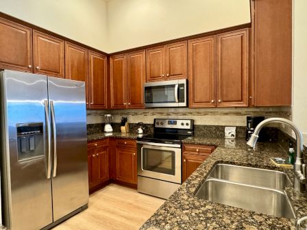 A kitchen with stainless steel appliances, wooden cabinets, granite countertops, and a double sink.