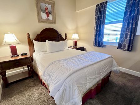 A cozy bedroom with a neatly made bed, lamps on side tables, patterned curtains, and a painting above the bed.