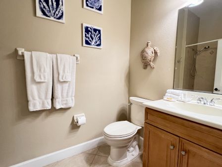 A bathroom with a toilet, towel rack with towels, seashell decor, and a sink with a mirror and toiletries on the countertop.
