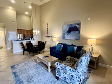 A modern living and dining area features a blue sofa, patterned chair, dining table, kitchen, and abstract wall art, creating a cozy ambiance.