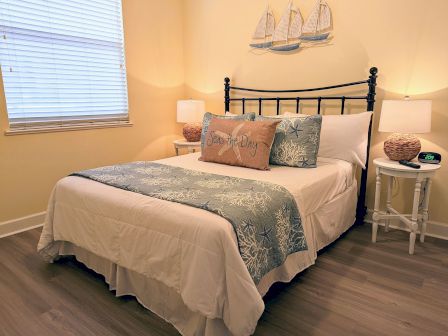 A neatly made bed with nautical-themed decor, lamps on side tables, and wall art featuring sailboats.