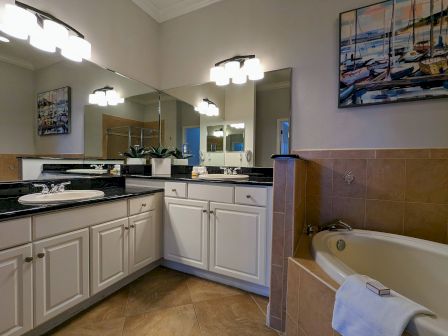 A bathroom with white cabinets, black countertops, a corner bathtub, mirrors, and nautical artwork on the wall.