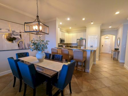 A modern dining and kitchen area with a table, blue chairs, art, pendant light, and bar stools.
