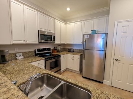 A kitchen with white cabinets, stainless steel appliances, granite countertops, and a double sink.