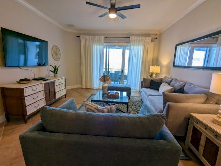 A cozy living room with a TV, couches, a coffee table, plants, and a sliding door with curtains, creating a well-lit and inviting space.