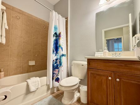 A bathroom featuring a tub with a colorful shower curtain, toilet, wooden vanity, mirror, and towels neatly arranged.