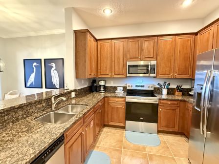 A kitchen with wooden cabinets, granite countertops, stainless steel appliances, and blue heron artwork.