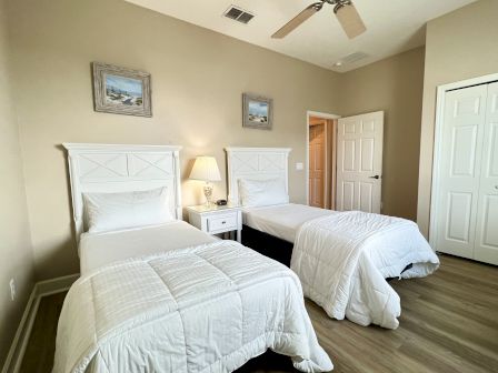 A bedroom with two twin beds, white bedding, a nightstand with a lamp between them, and two framed pictures above the headboards.