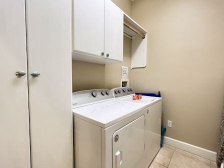 A laundry room with a washer, dryer, cabinets, and a shelf with detergent.